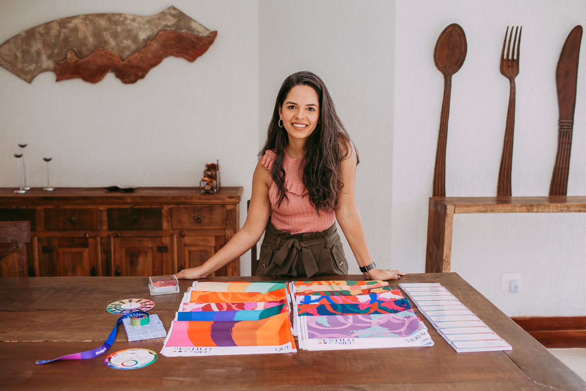 A smiling designer with colorful fabric samples displayed on a table in a modern studio setting.