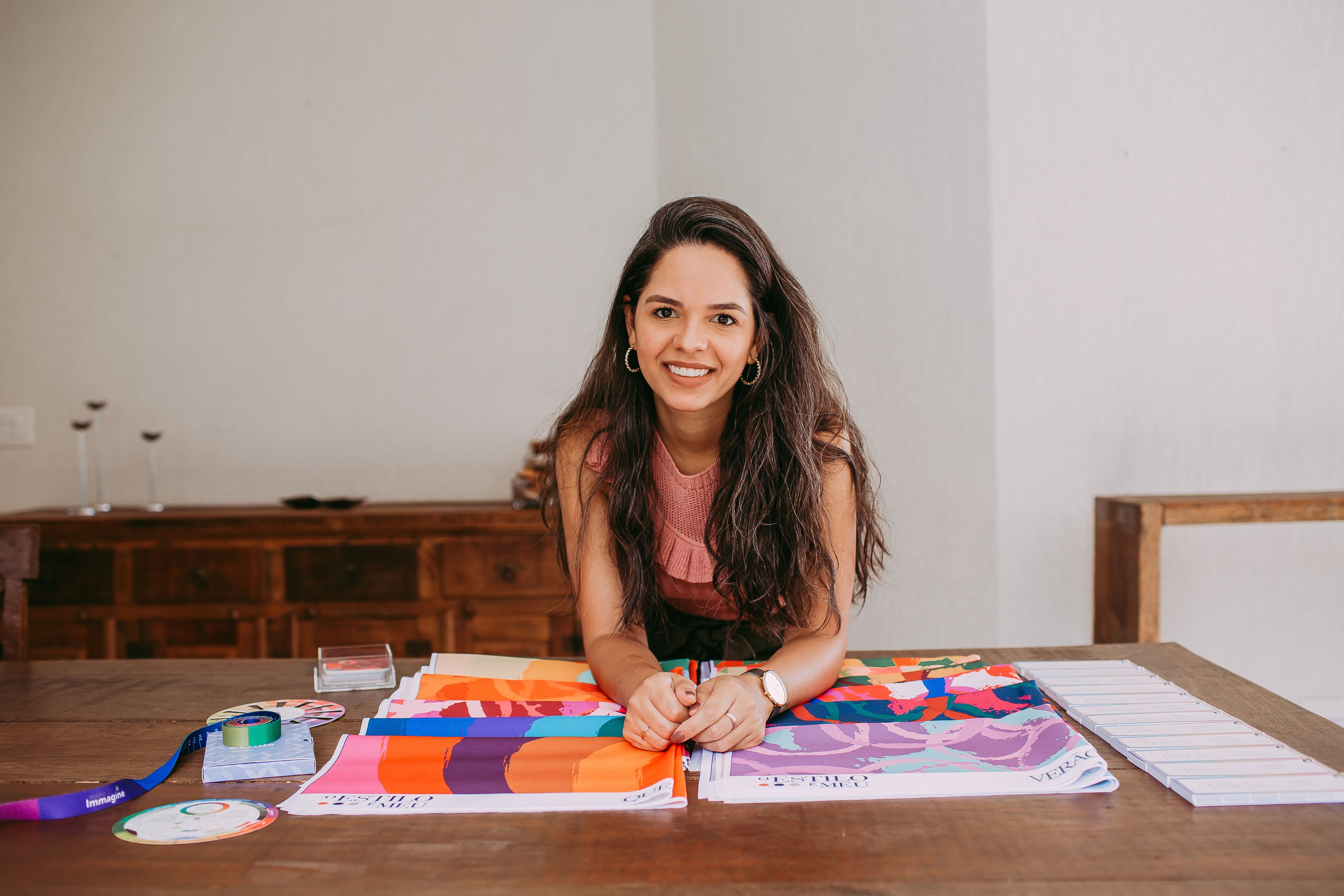 A woman smiling while showcasing vibrant fabric samples on a wooden table indoors.
