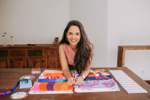 Free Young woman designer smiling at her workspace with colorful fabric samples and design tools on the table. Stock Photo