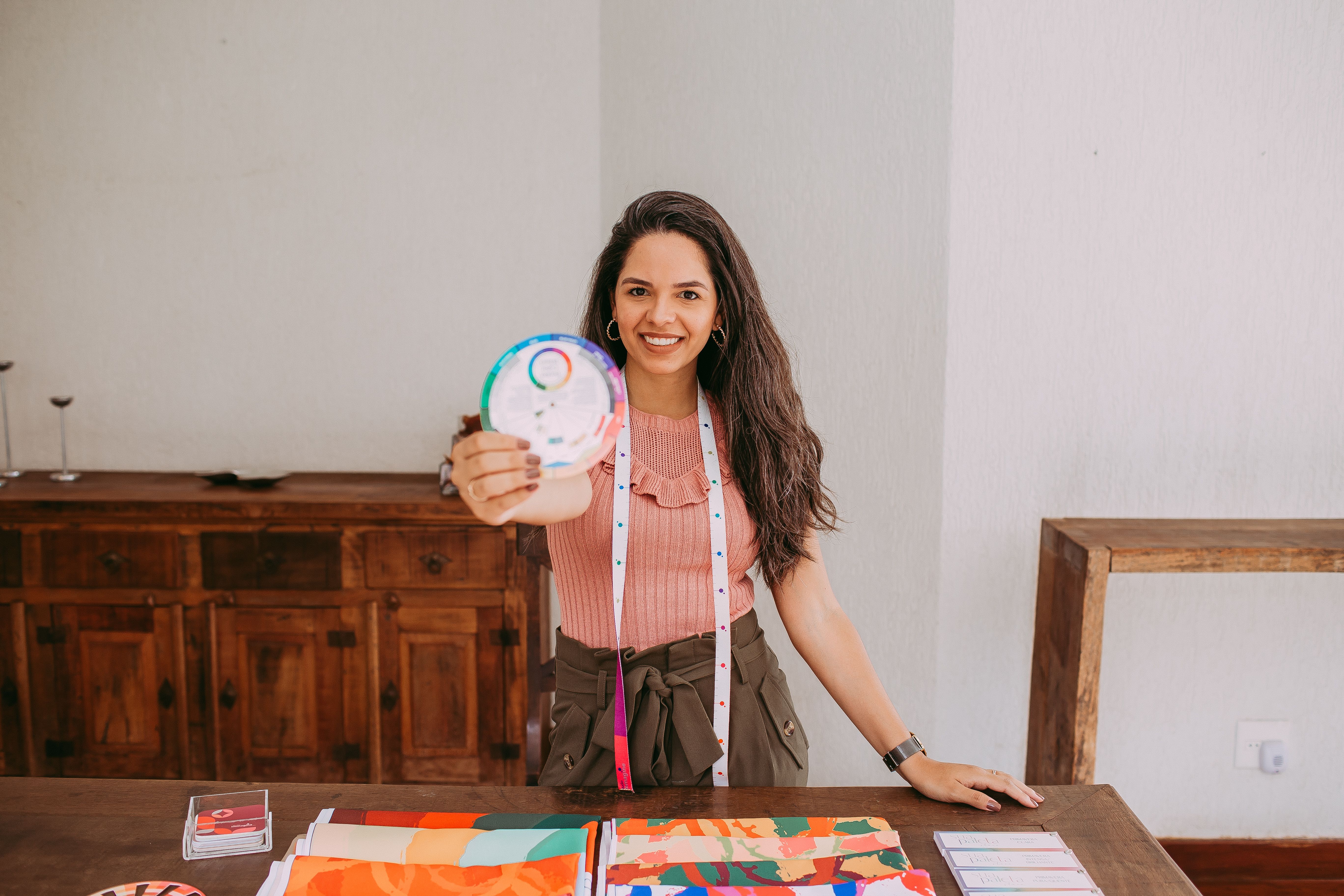 Smiling woman displaying a color wheel at a table with fabric samples in a workshop setting.