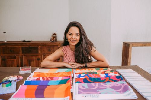 Free A smiling woman with long hair sits at a table with colorful fabric samples indoors. Stock Photo