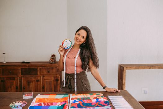 A Woman in Pink Top with Tape Measure Around Neck Holding a Color Pallet Beside Table