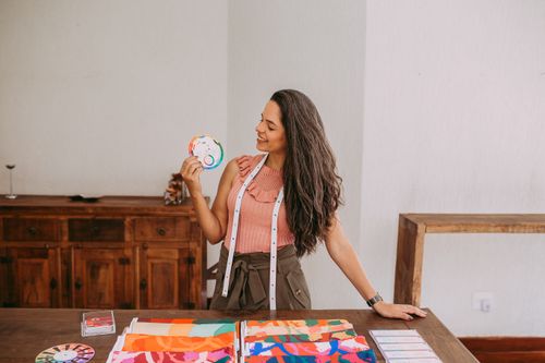 Free A smiling woman designer with fabric samples and measuring tape in a creative workspace. Stock Photo