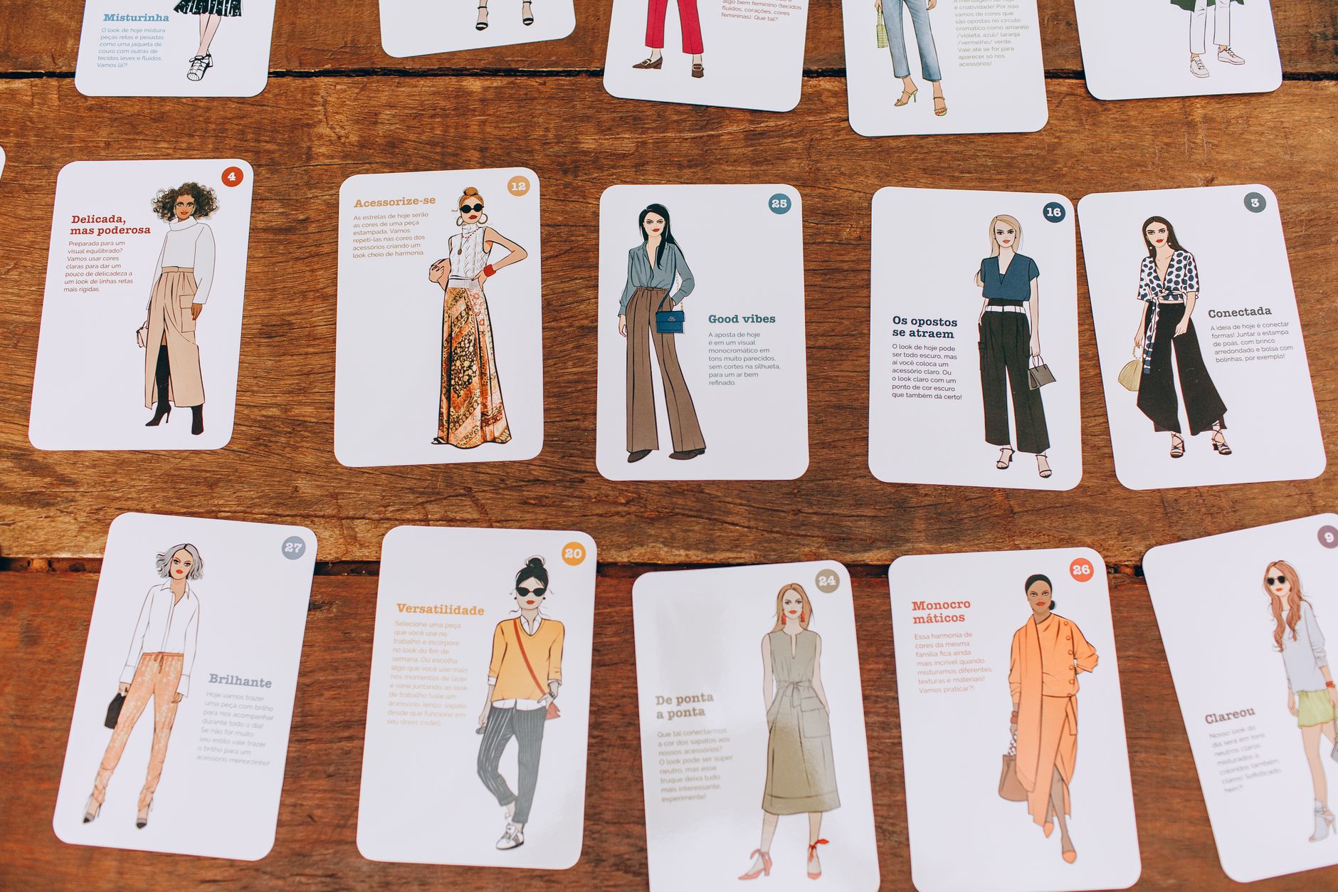 A collection of fashion illustration cards arranged on a wooden table, showcasing diverse styles.
