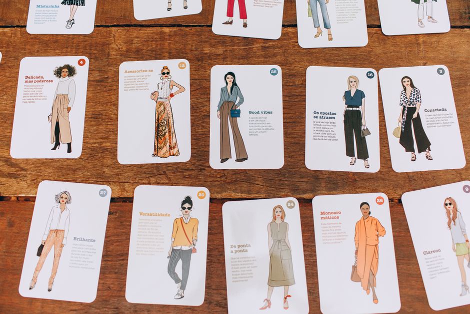 Como Encontrar seu Estilo Pessoal Através da Moda Sustentável 2 A collection of fashion illustration cards arranged on a wooden table, showcasing diverse styles.