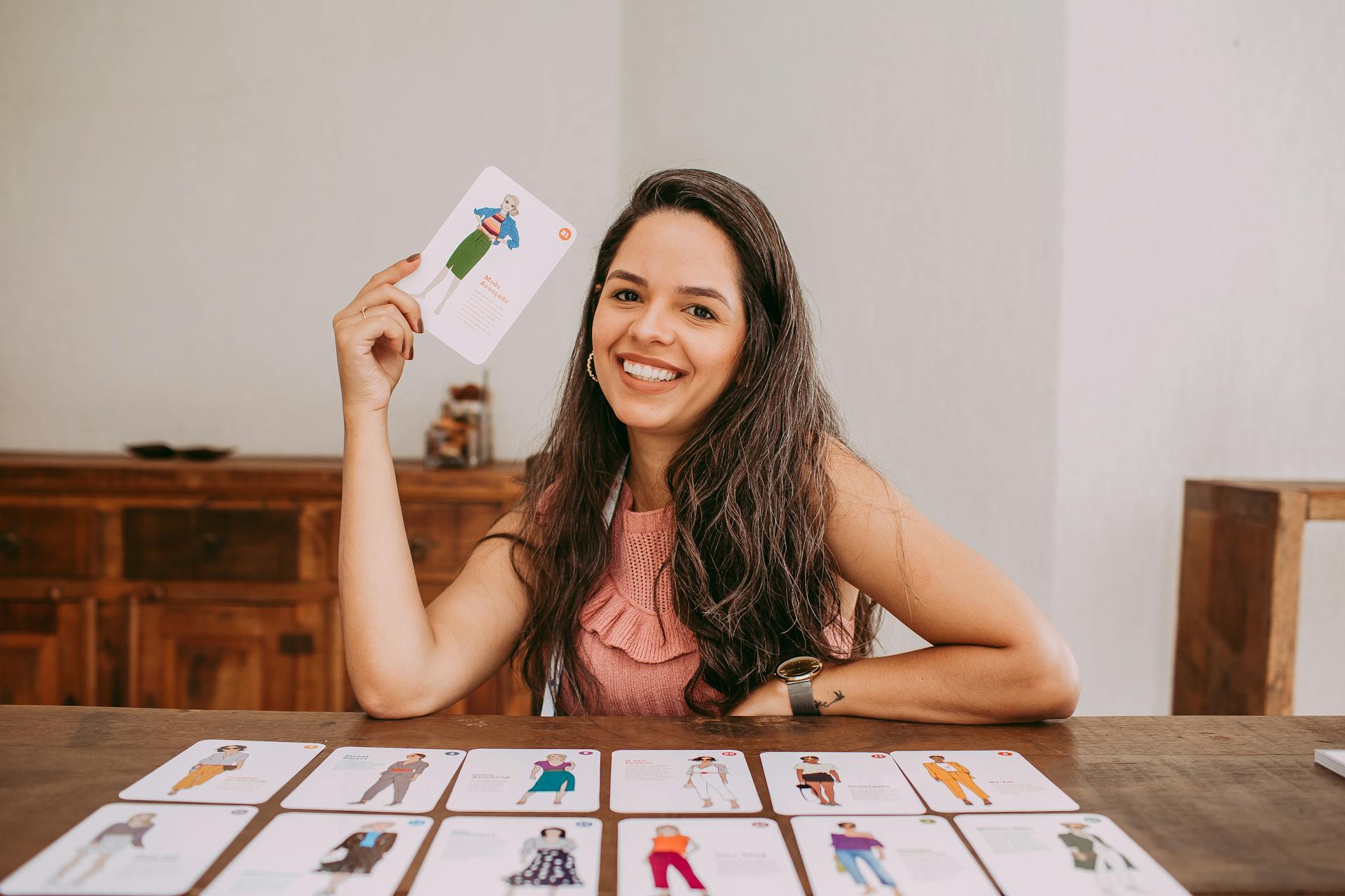 A cheerful woman holding a card while sitting at a table filled with game cards.