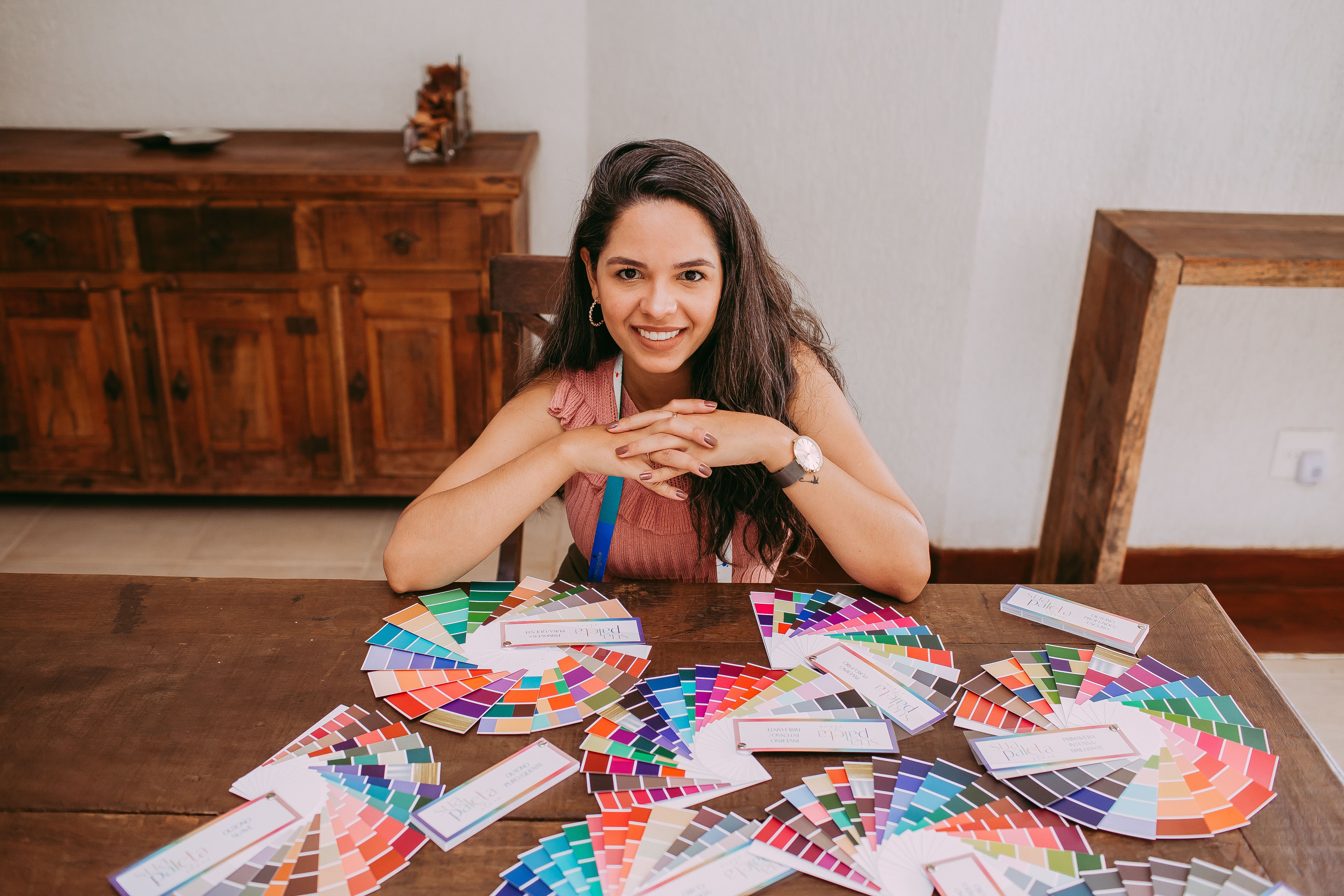 A smiling woman sits at a table with colorful swatches indoors, surrounded by a warm ambiance.