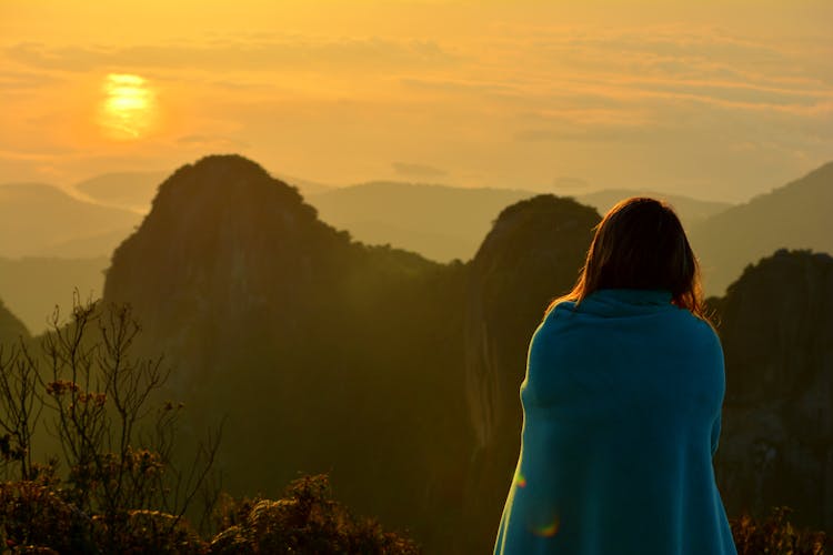 Back View Of A Person Wrapped In Blue Blanket Looking At A Scenic View