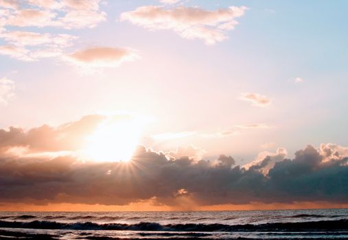 Stunning sunrise over ocean waves with dramatic clouds and bright sunlight.