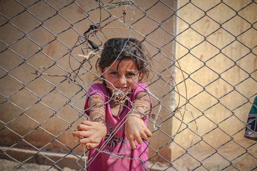 Free Portrait of a young girl reaching through a broken chain-link fence in Idlib, Syria. Stock Photo