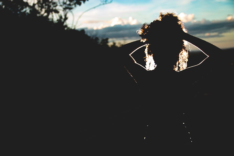 Silhouette of a woman with curly hair against a colorful sunset sky.