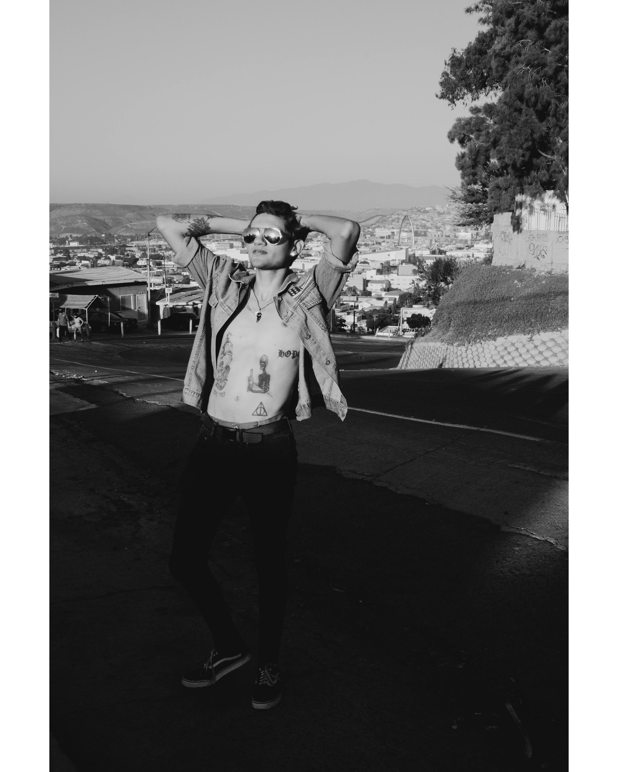 Free Black and white image of a tattooed man posing on a street in San Diego cityscape. Stock Photo