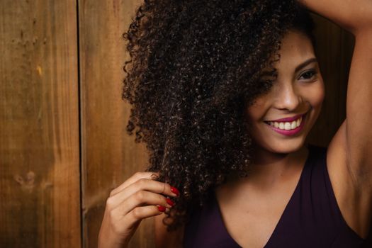 Close-up portrait of a smiling woman with curly hair touching her locks indoors.