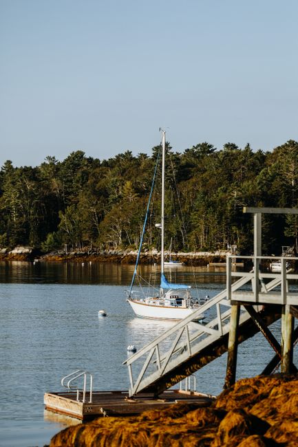 Tranquil scene of a sailboat anchored by a wooded shore and pier on a clear day.