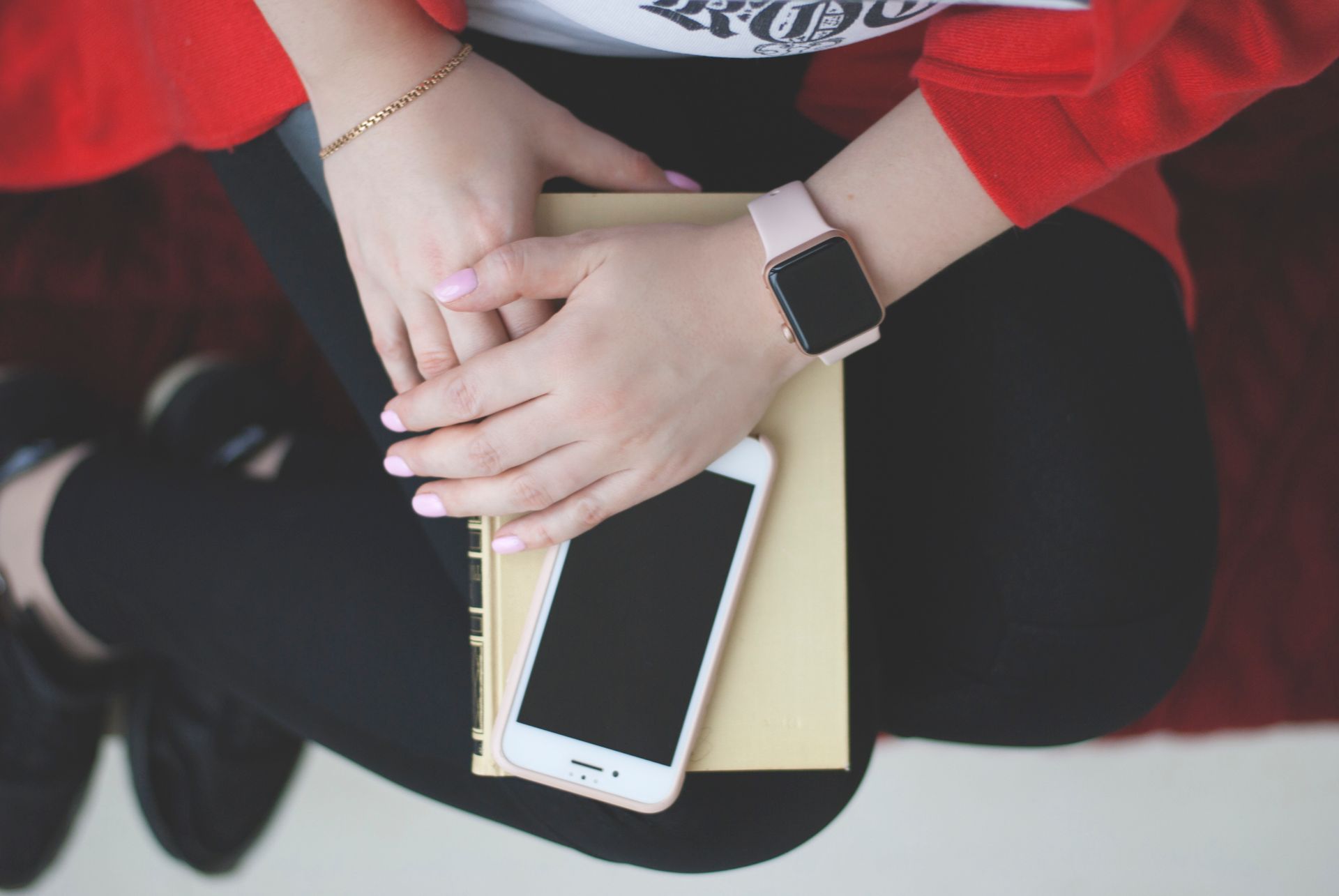 Woman's hands with a watch resting on a book and smartphone, view from above.