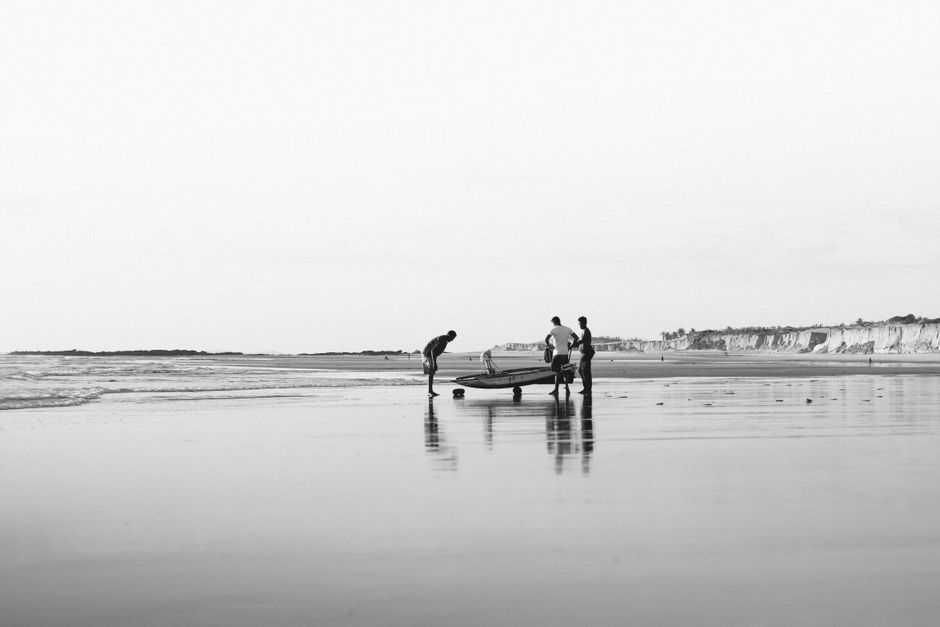 Black and white photo of fishermen with a boat on Canoa Quebrada beach reflecting on wet sand.