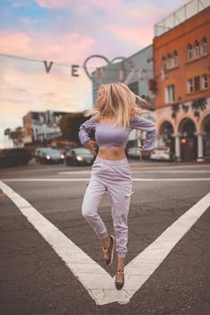 Energetic woman in trendy outfit jumps across the street at Venice Beach at sunset.
