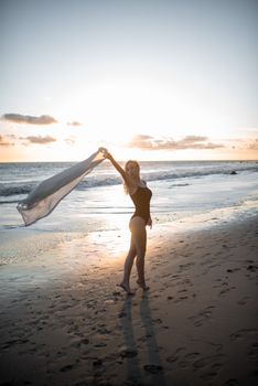 Woman in swimsuit enjoying a beautiful sunset on a serene beach with ocean waves and golden sky.