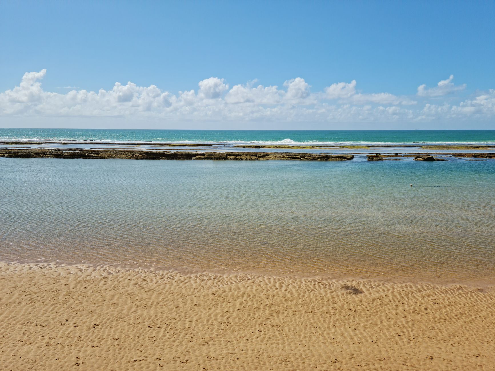 Peaceful sandy beach and calm ocean with rippling waves under a clear blue sky.
