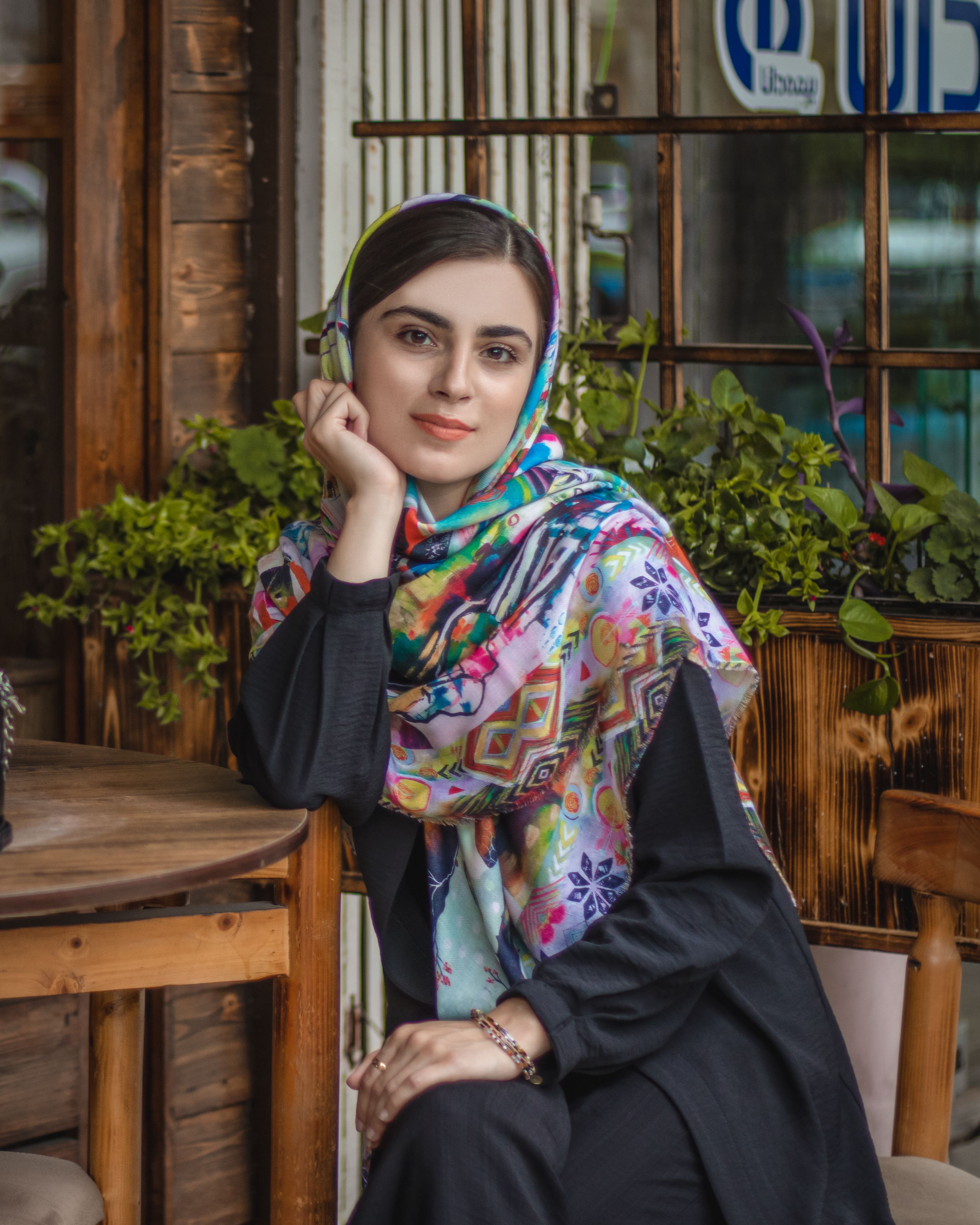 Stylish Middle Eastern woman in vibrant hijab, sitting at an outdoor cafe in Iran.