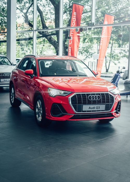 Free Bright red Audi Q3 displayed in a modern car showroom with promotional banners. Stock Photo