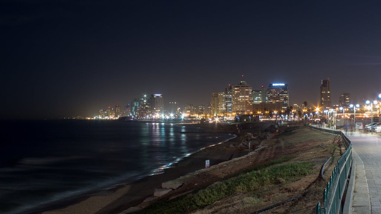 Free Grey Concrete Way Near Body of Water Leading to City during Nighttime Stock Photo