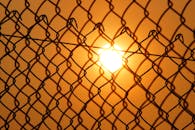透过铁丝网围栏拍摄日落，形成戏剧性的剪影效果