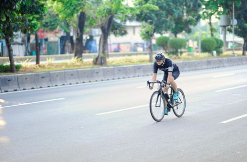 Free A cyclist rides along an empty urban road surrounded by greenery in Jakarta. Stock Photo