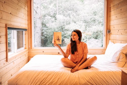 Free A Woman Reading a Book while Sitting on the Bed Stock Photo