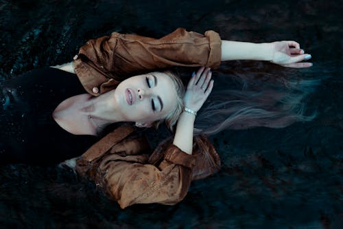 Free A Woman in a  Brown Jacket Lying on Water Stock Photo