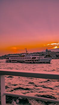 A ferry boat sails across the Bosphorus in Istanbul under a vivid sunset, creating a picturesque scene.