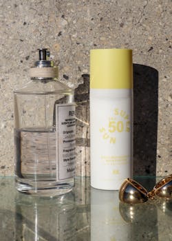 Sunscreen and perfume bottles with sunglasses on a sunny day, evoking summer vibes.