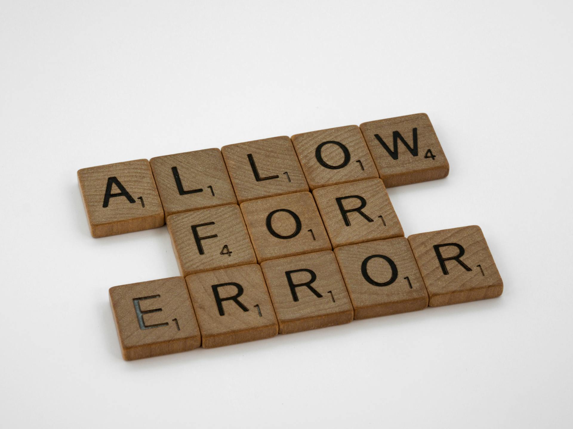 Wooden Scrabble tiles spelling 'Allow for Error' on a white surface.