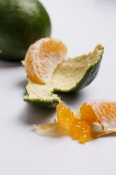 Close-up of a fresh orange with its green peel, showcasing juicy segments on a white background.