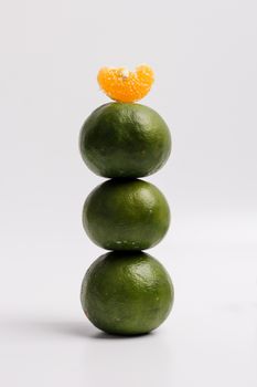 Creative stack of three green citrus fruits topped with an orange slice against a white background.