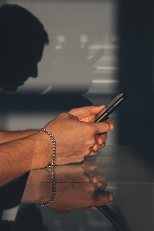 Free Man's Hand Wearing Chain Bracelet Holding a Black Phone Stock Photo