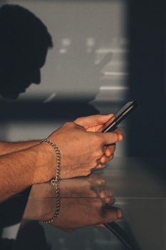 A man wearing a bracelet holds a smartphone with shadows and reflections visible.