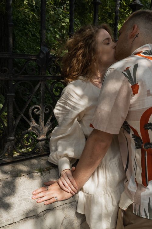 Free An intimate moment of a couple kissing by a metal fence in a sunlit outdoor setting. Stock Photo