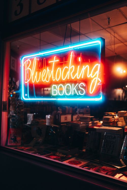 Free Illuminated neon sign of Bluestocking Books glowing in a cozy bookstore setting. Stock Photo