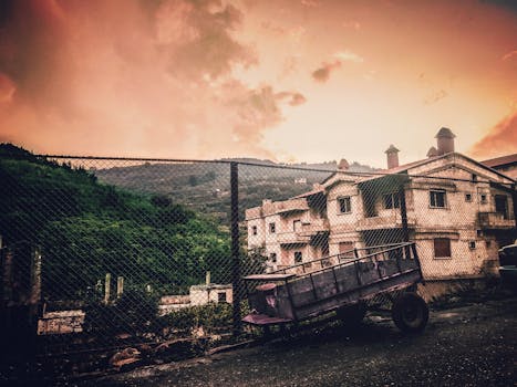 A rural landscape with houses, trailer, and vibrant sky during sunset.