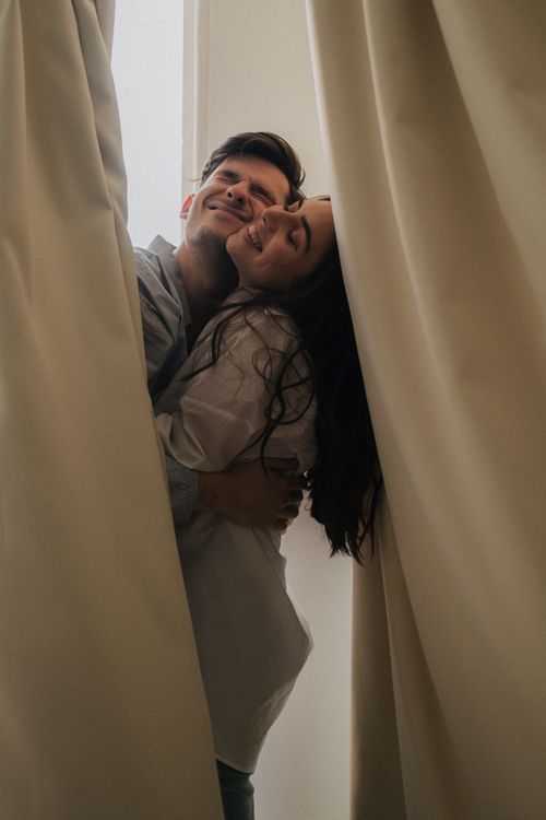 Free Loving couple sharing an intimate hug by a window, surrounded by drapes. Stock Photo