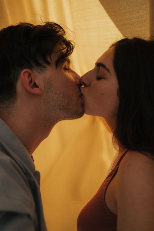 Free A romantic and intimate moment of a couple kissing indoors with soft, warm lighting. Stock Photo