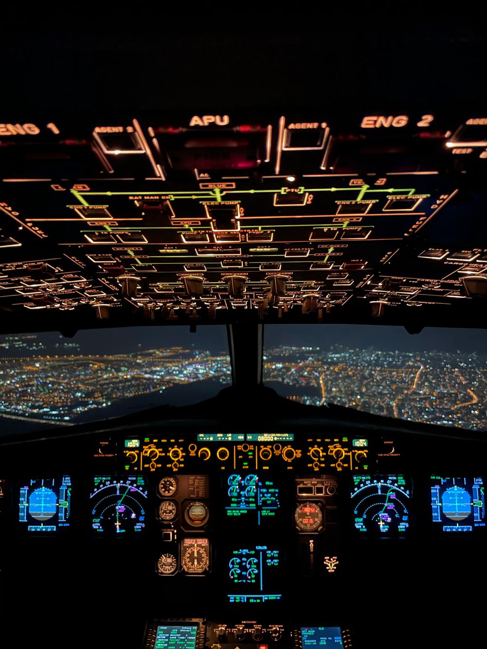 Aircraft cockpit displaying illuminated controls over a nighttime cityscape