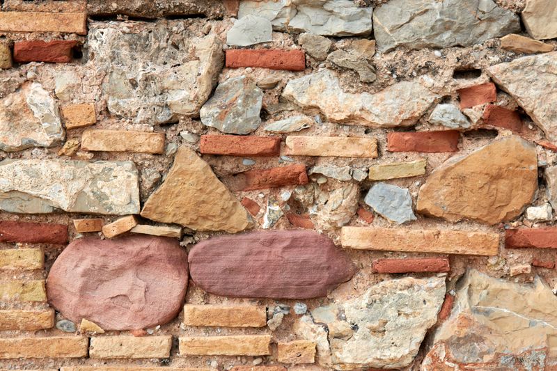 Detailed view of a rough textured stone and brick masonry wall, ideal for backgrounds.