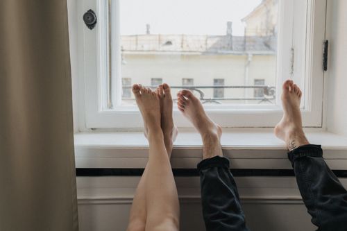 Free Two people lying barefoot on a windowsill, enjoying sunny relaxation indoors. Stock Photo