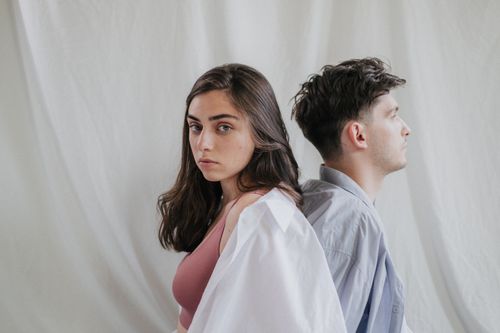 Free A couple sitting back to back in a minimalist setting, deep in thought. Stock Photo