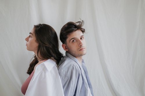 Free A thoughtful couple sitting back to back against a plain backdrop, conveying connection and contemplation. Stock Photo