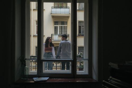 Free Couple enjoying a moment together on a balcony, framed by a window. Stock Photo