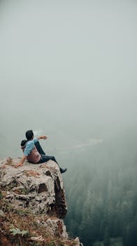 A lone adventurer sitting on a cliff edge, surrounded by a foggy forest view.