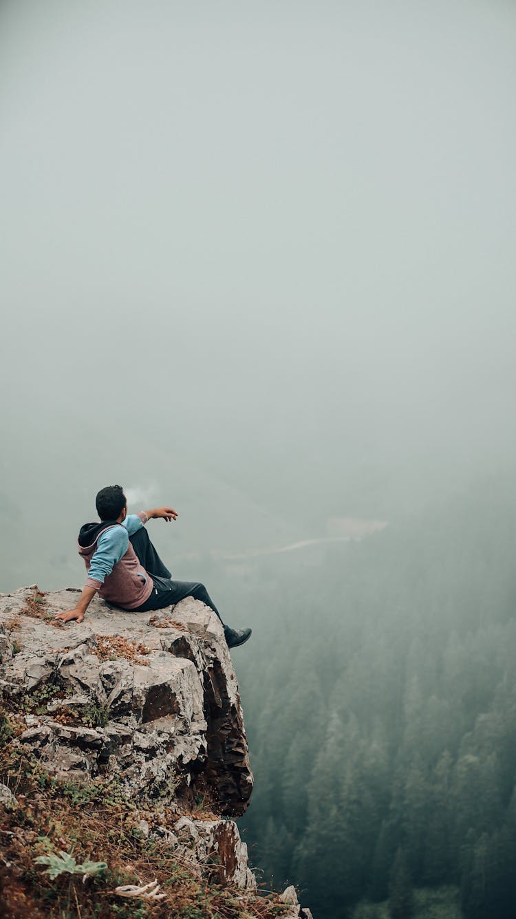 A Person Sitting At The Edge Of A Cliff